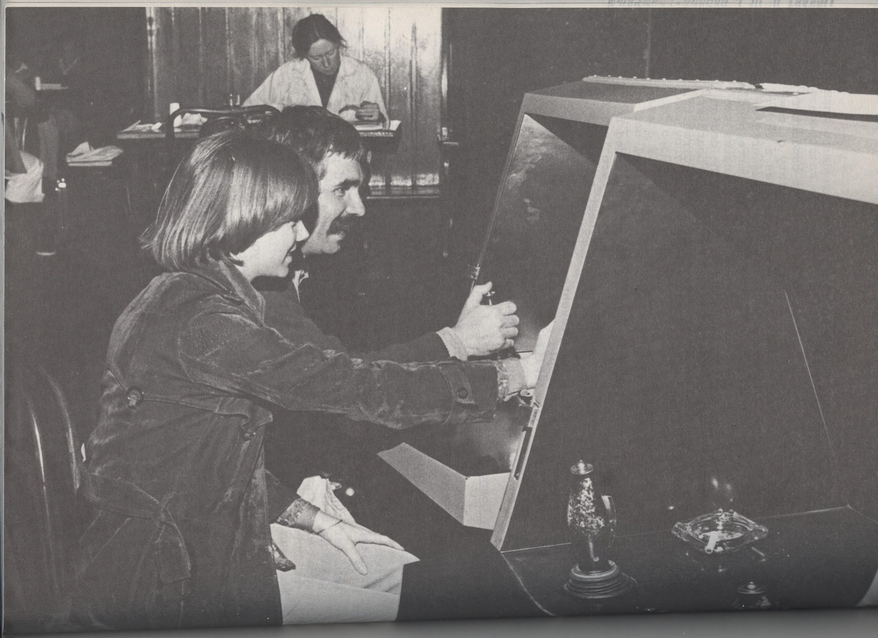 Period photograph of players at the angular early cabinet. The January 1977 publication date is not the exposure date.